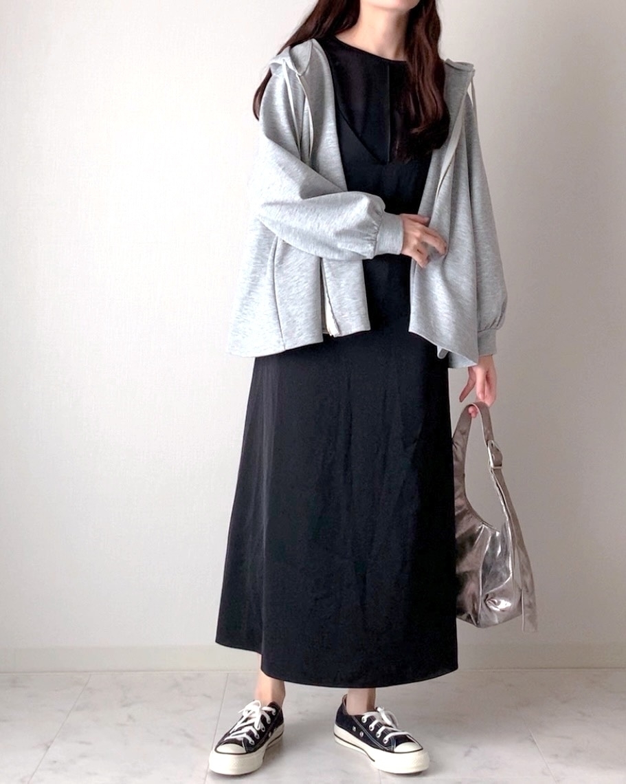 女性がカジュアルなフード付きジャケットと黒いロングワンピースを着用し、スニーカーを履いて立っている。