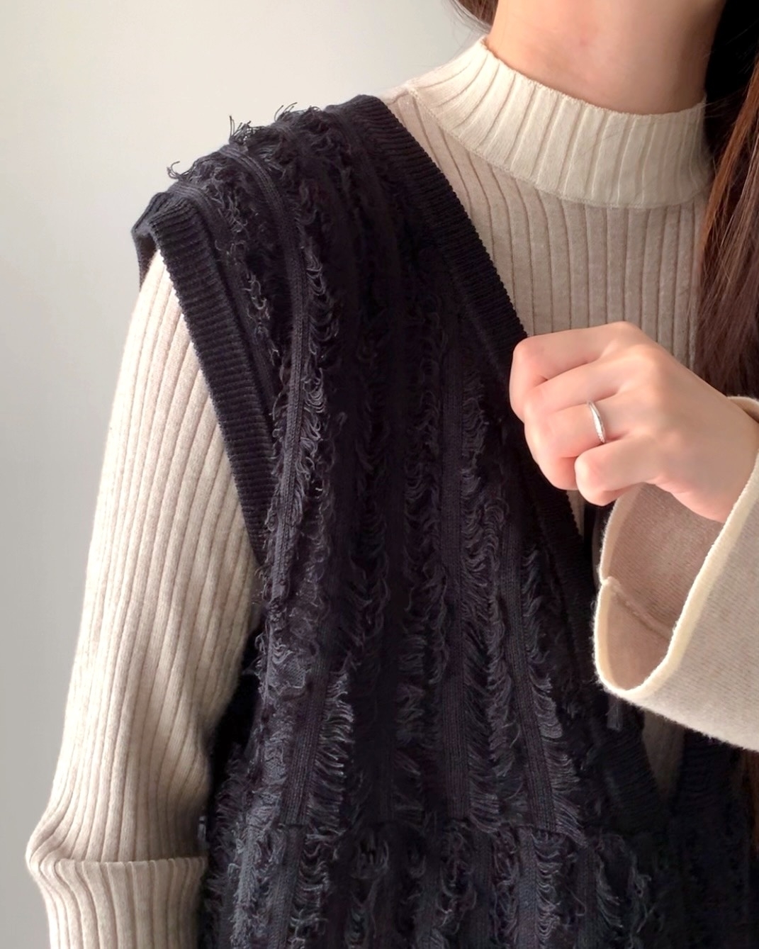 女性がリブニットの上にざっくり編まれたベストを重ねて着用している。指にはシンプルなリング。
