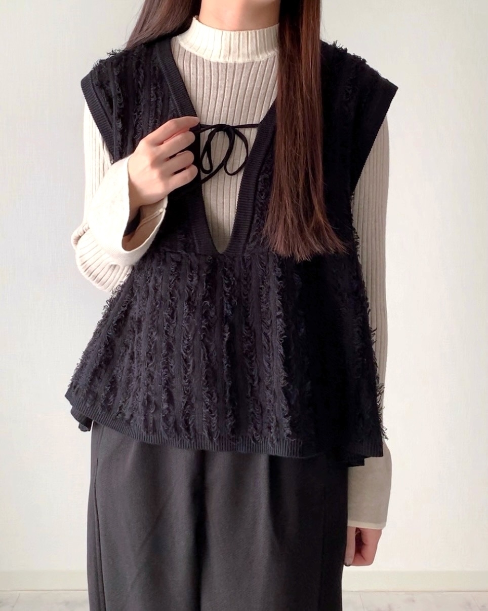 女性がゆったりしたセーターと編み込まれた黒いベストを着ている。カジュアルでリラックスしたファッションスタイル。