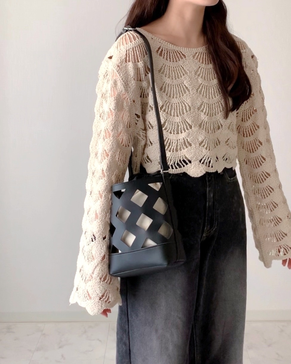 女性がニットトップスと黒のワイドパンツを着用し、デザインバッグを肩に掛けている。顔は写っていない。