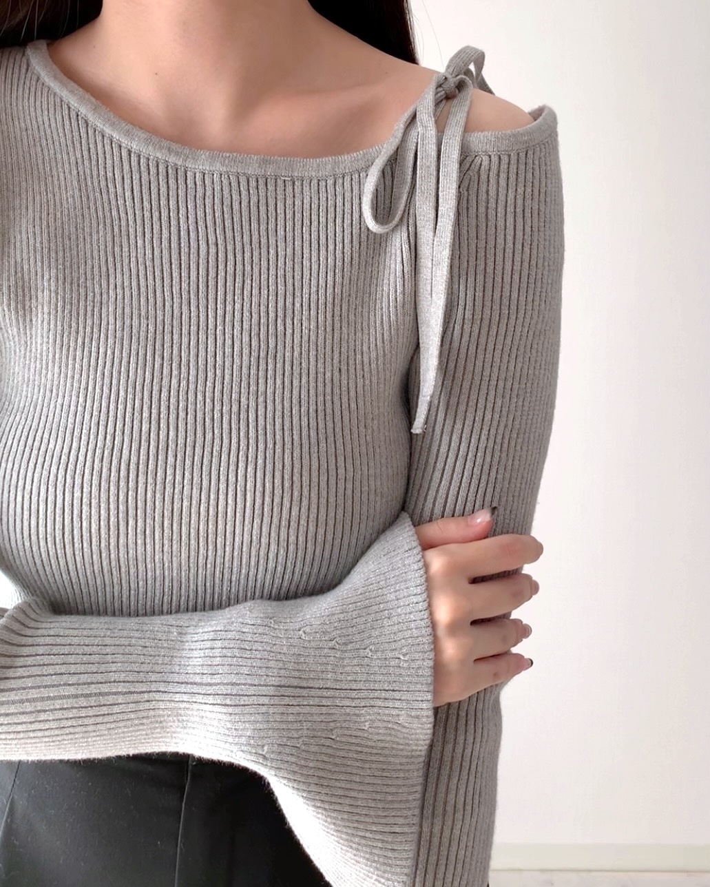 女性が長袖のリブニットを着て腕を組んでいる。ニットは肩部分にリボンの飾りがある。