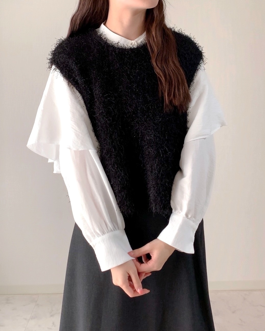 女性が白いシャツにふわふわの黒いベストを重ね着し、スカートを着ています。