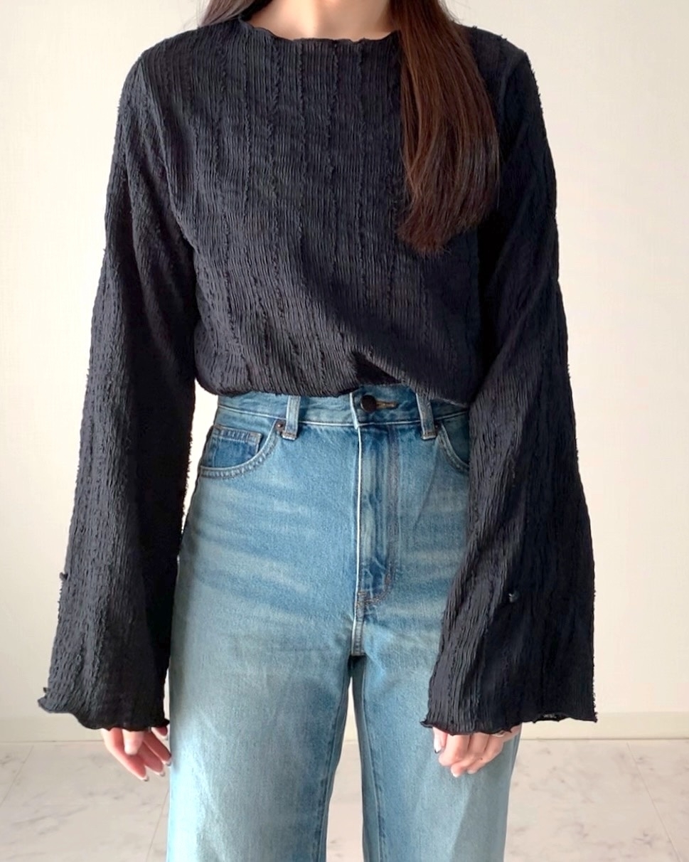 女性が長袖の黒いトップスとデニムパンツを着用している。シンプルでカジュアルなファッション。