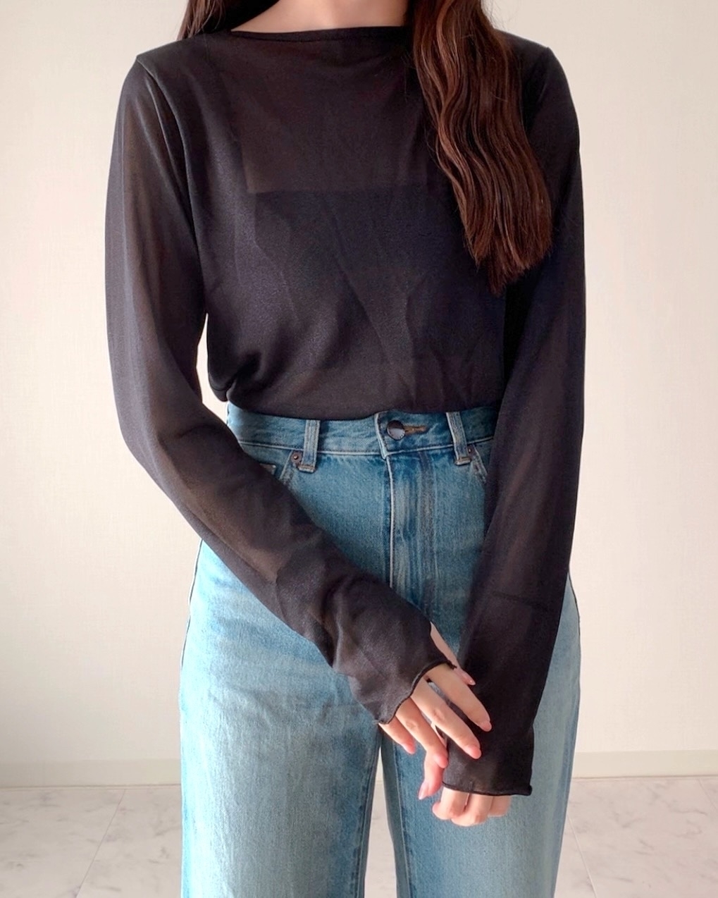 ゆったりフィットの黒い長袖トップスとデニムジーンズを着た人物。顔は写っていない。リラックスしたポーズで立っている。