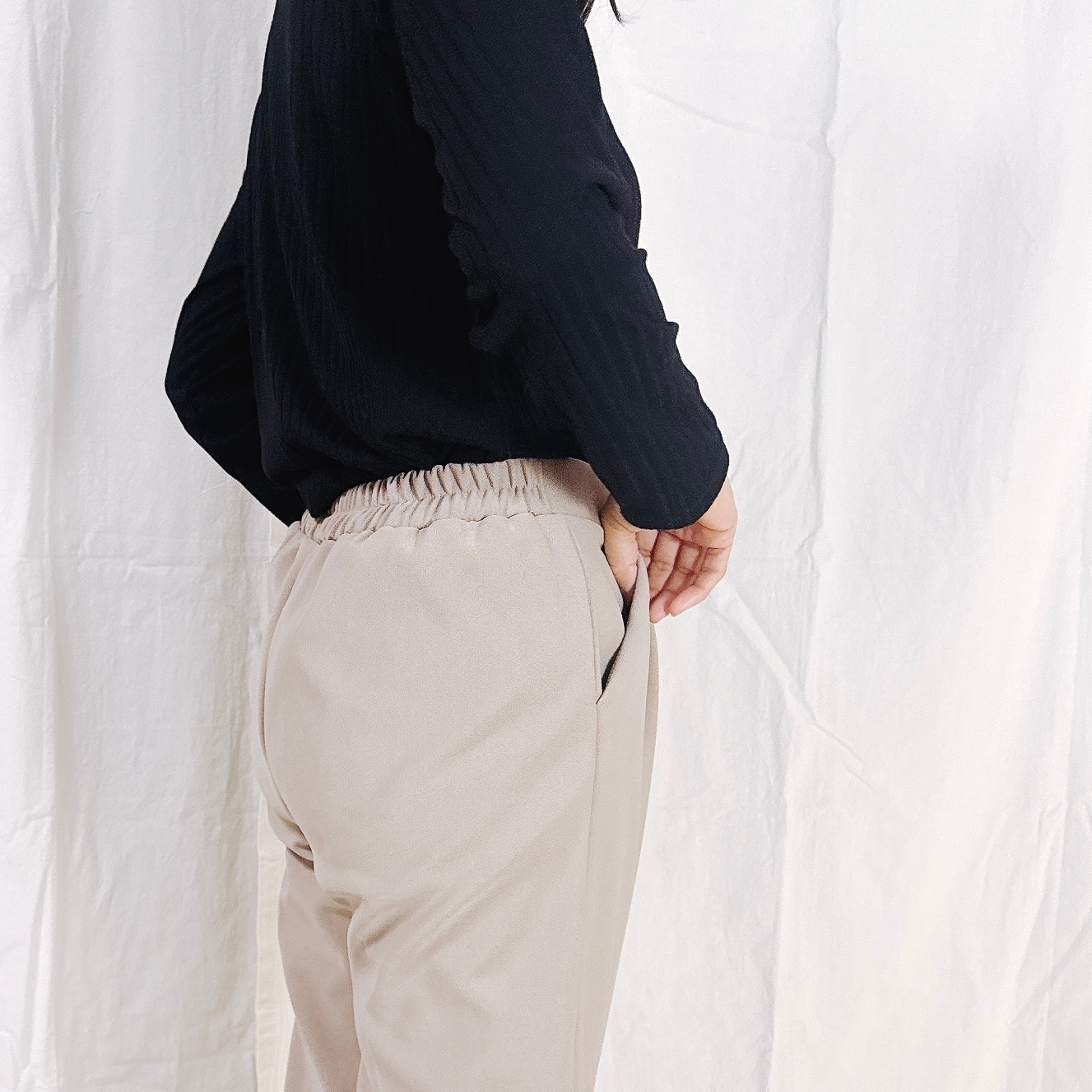 横向きに立っている人が黒いトップスとベージュのパンツを着用。手はポケットに差し込まれています。