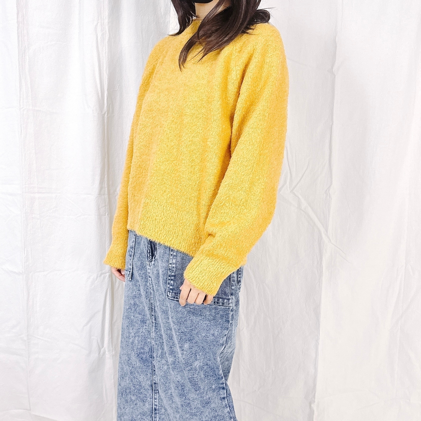 女性がゆったりとしたジーンズとセーターを着て立っている様子。カジュアルなファッションスタイル。