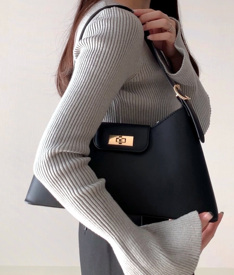 女性がリブの長袖トップスを着て、大きなバッグを持っている横向きの姿。