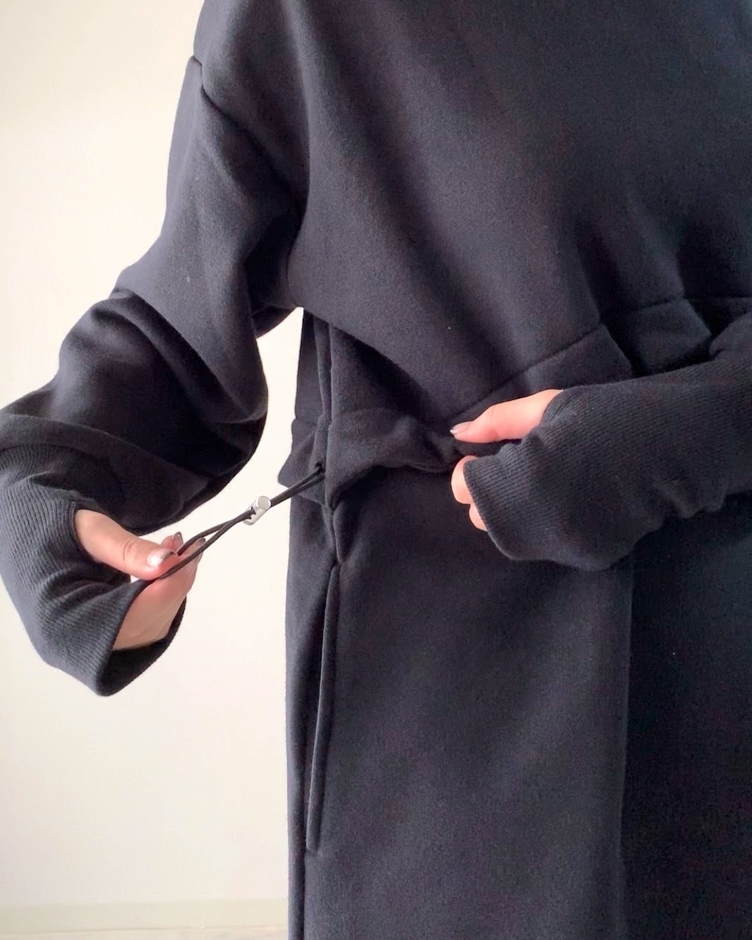 黒いシンプルなコートを着た人がベルトを調整している手元の様子。