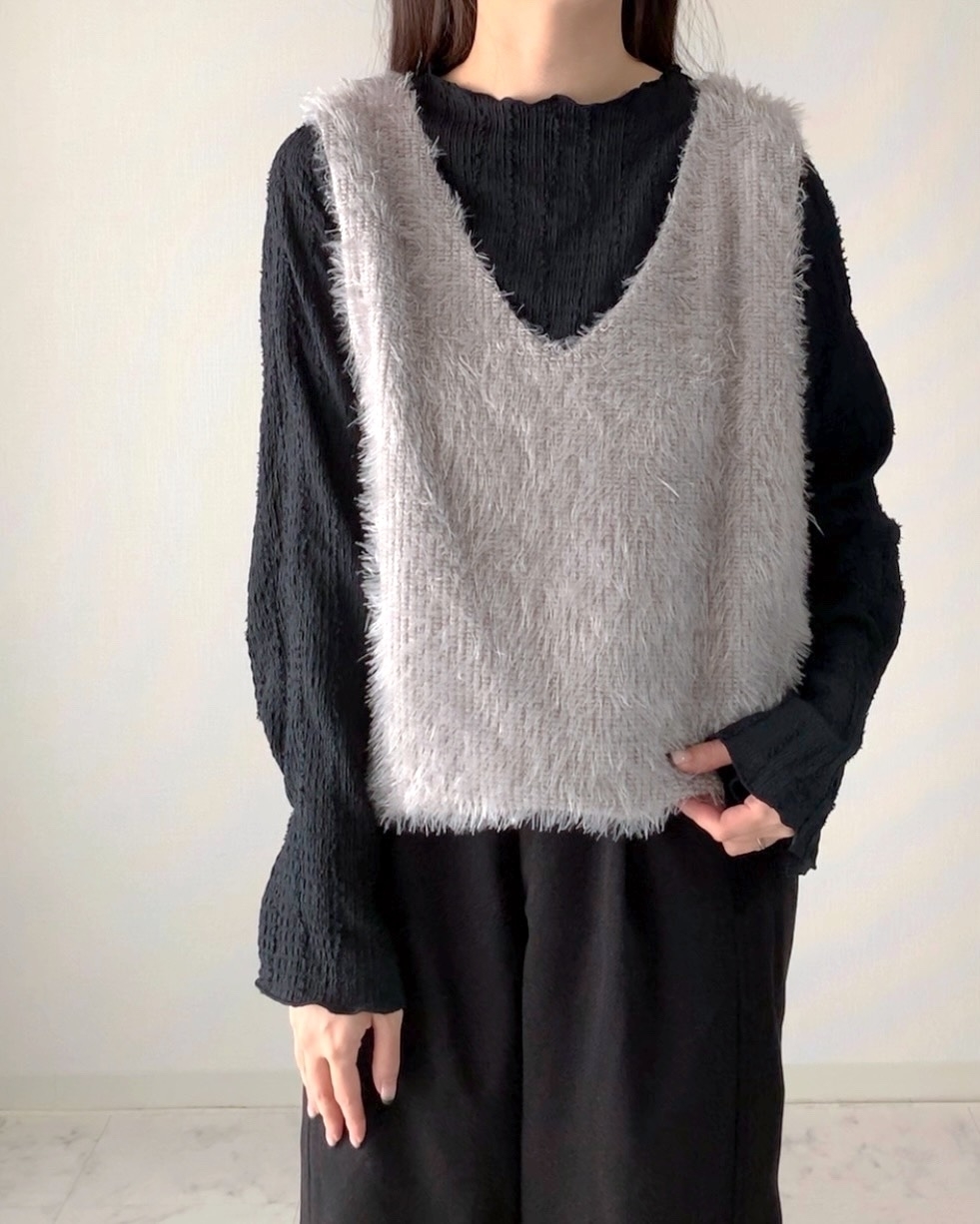 女性が長袖の黒いシャツの上に毛羽立ったグレーのベストを着用している。