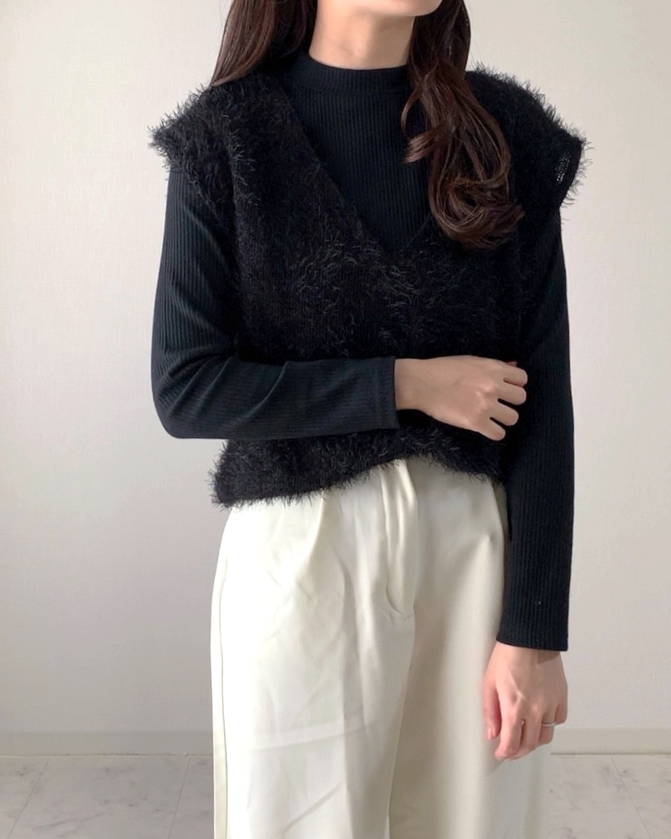 女性が黒のトップスとファー付きベスト、白のパンツを着てポーズ。顔は見えない。