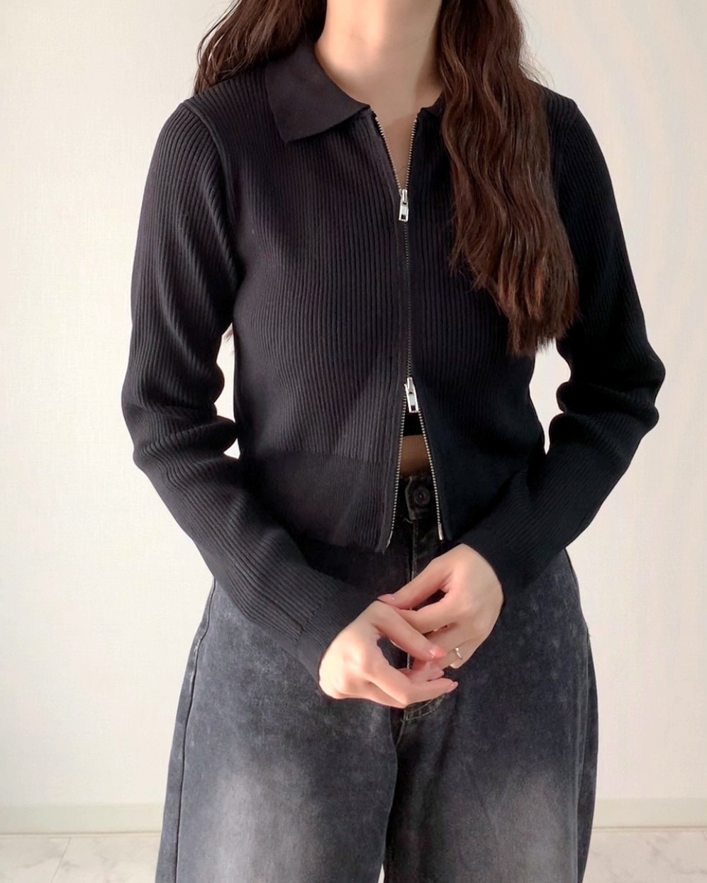 女性が長袖のジップアップトップスとデニムパンツを着用している。
