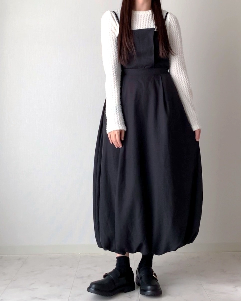 白いニットと黒いサロペットドレスを着た女性が立っている。クラシックでシックなスタイル。