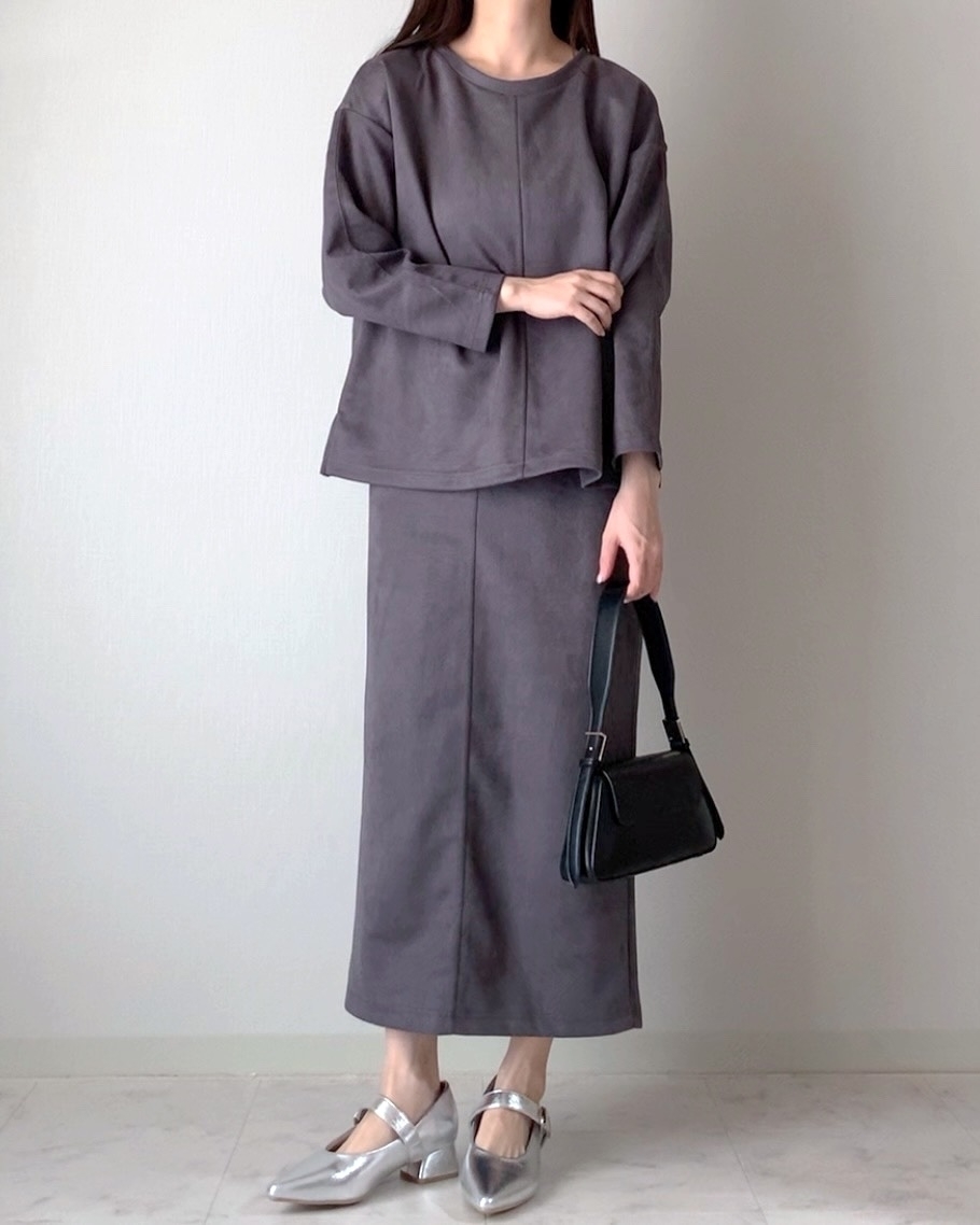 ゆったりしたトップスとロングスカートを着た人が黒のハンドバッグを持ち、銀色のシューズを履いている。
