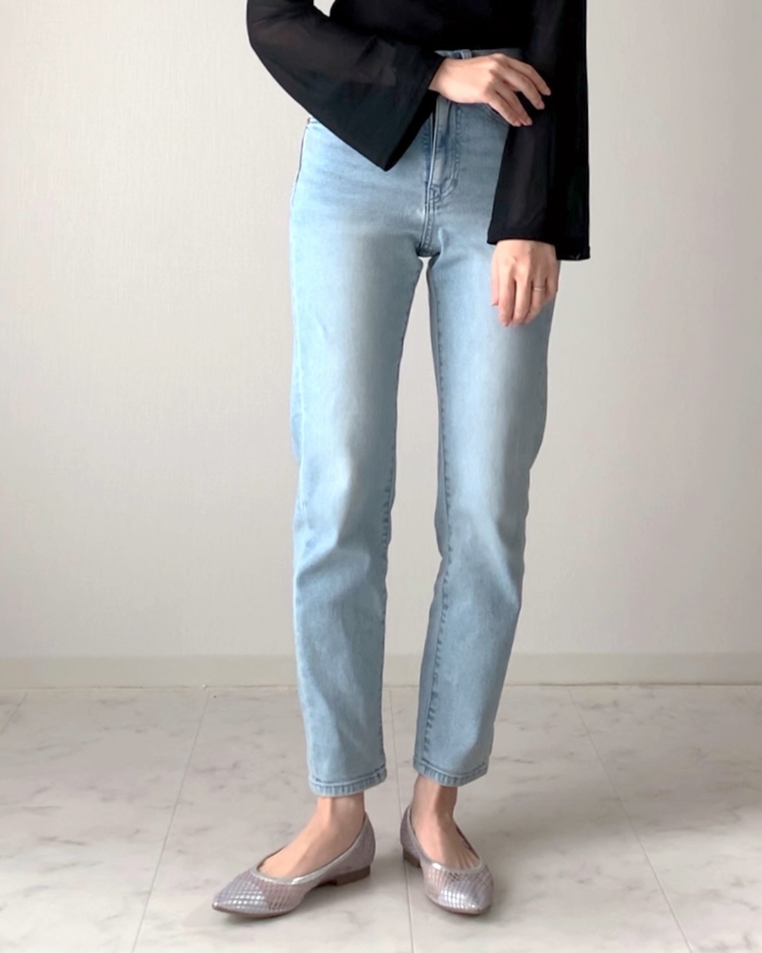 女性が長袖のトップスとジーンズを着用し、足元にはフラットシューズを履いている。