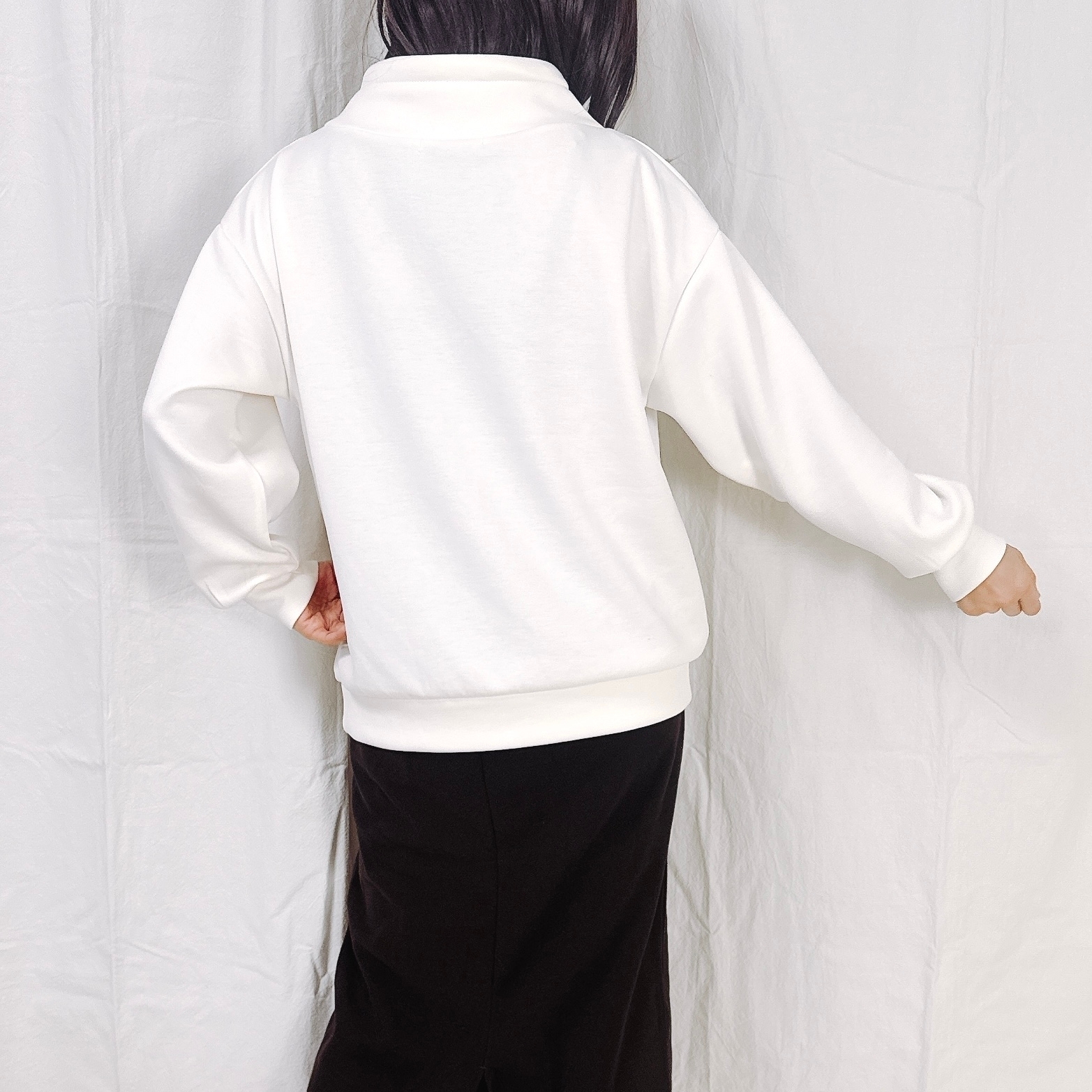 背を向けた人がシンプルな白いシャツと黒いパンツを着ています。