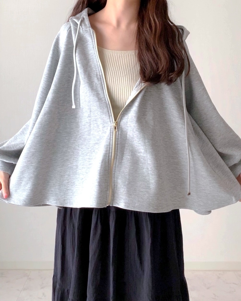 女性がゆったりしたジッパーフード付きトップスとスカートを着ている。