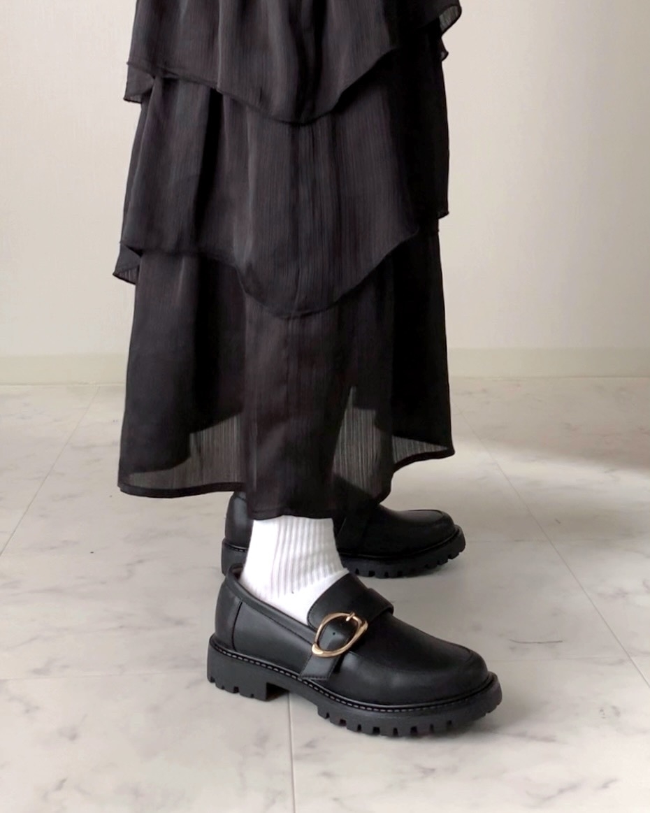 黒いローファーと白いソックスを履いた脚が、長い黒いティアードスカートの下から見える。