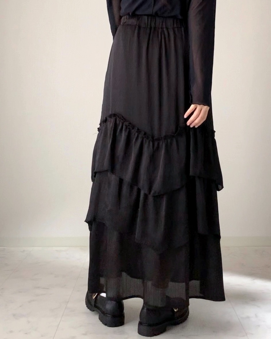 黒のフリルスカートとブーツを身に着けた人が立っている。スカートは階層状のデザイン。