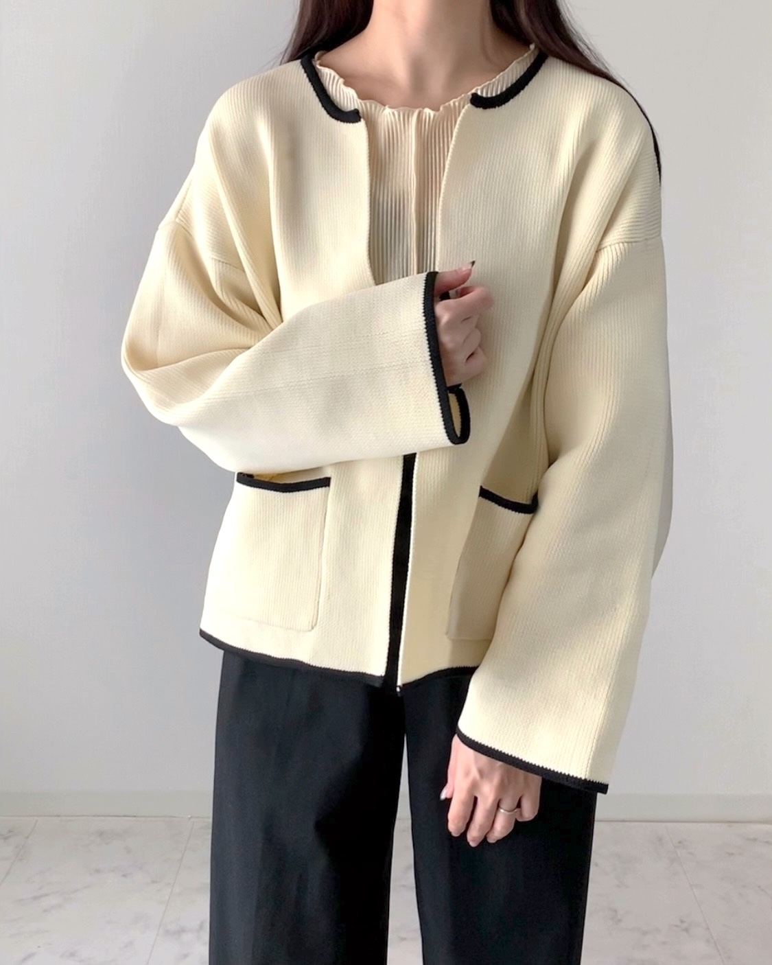 ゆったりしたトップスと黒パンツを着た人物が立っている。トップスはリブ編みで、シンプルなデザインです。