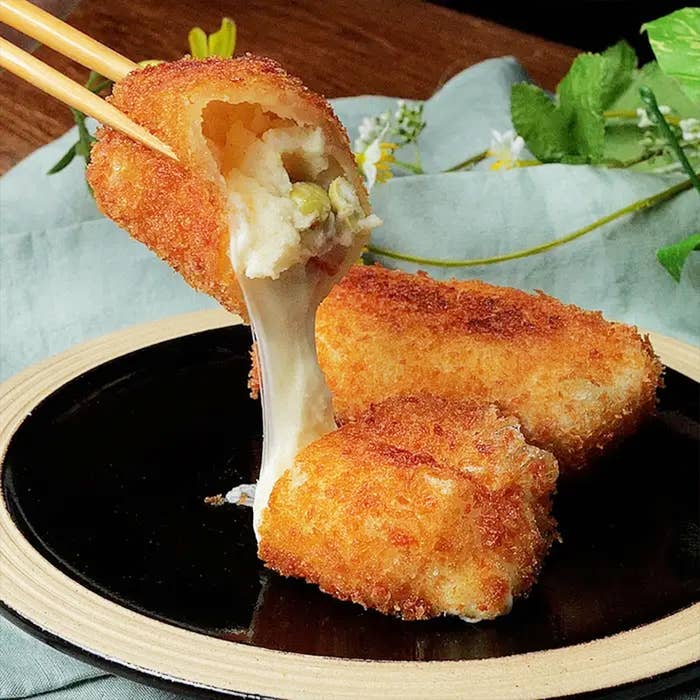 チーズとエンドウ豆入りの揚げたコロッケが箸で割られ、中からとろけるチーズが伸びている。