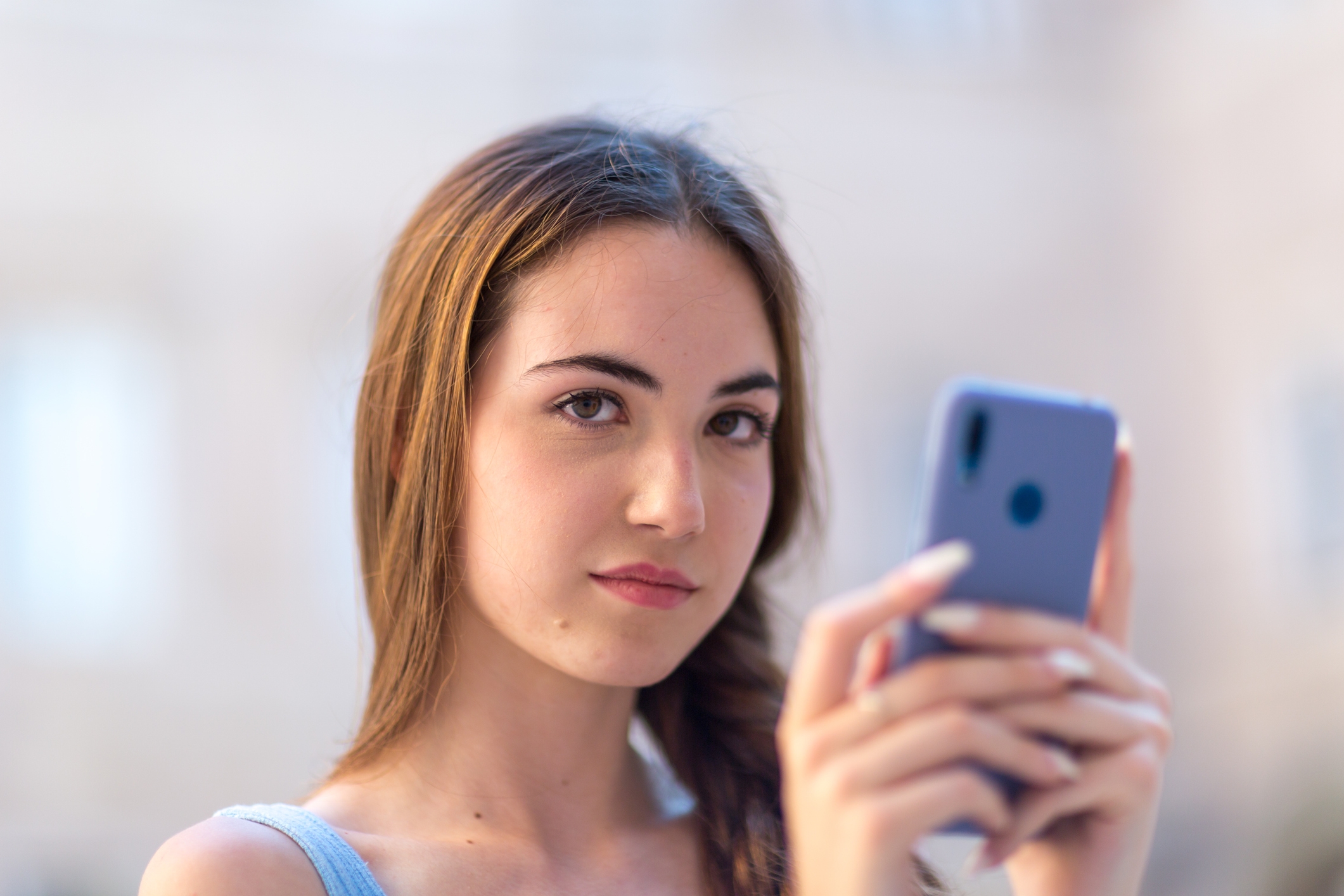 Personen som holder en smarttelefon, ser mot kameraet med et nøytralt uttrykk