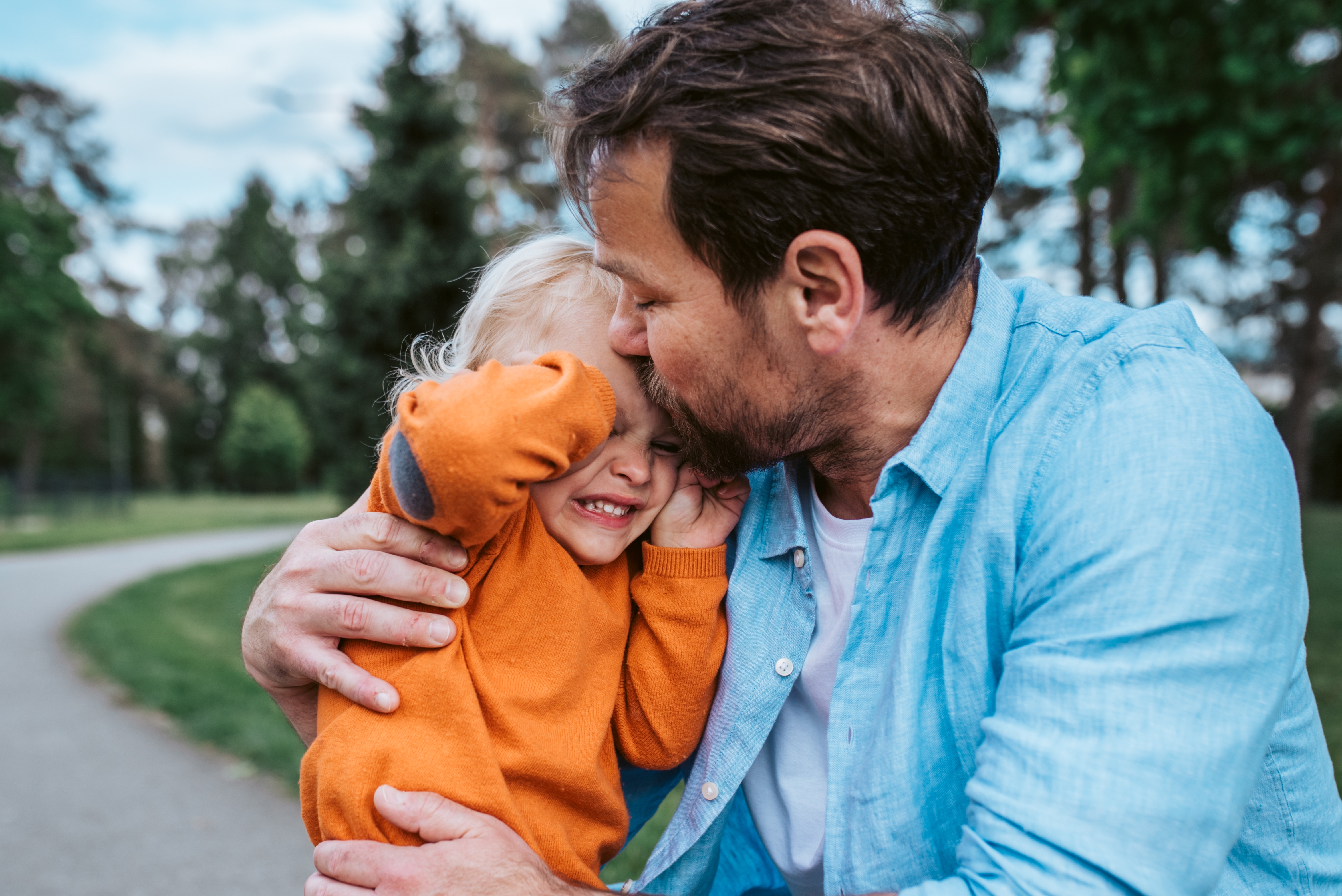 Foreldre som klemmer et smilende barn i en park, formidler varme og kjærlighet
