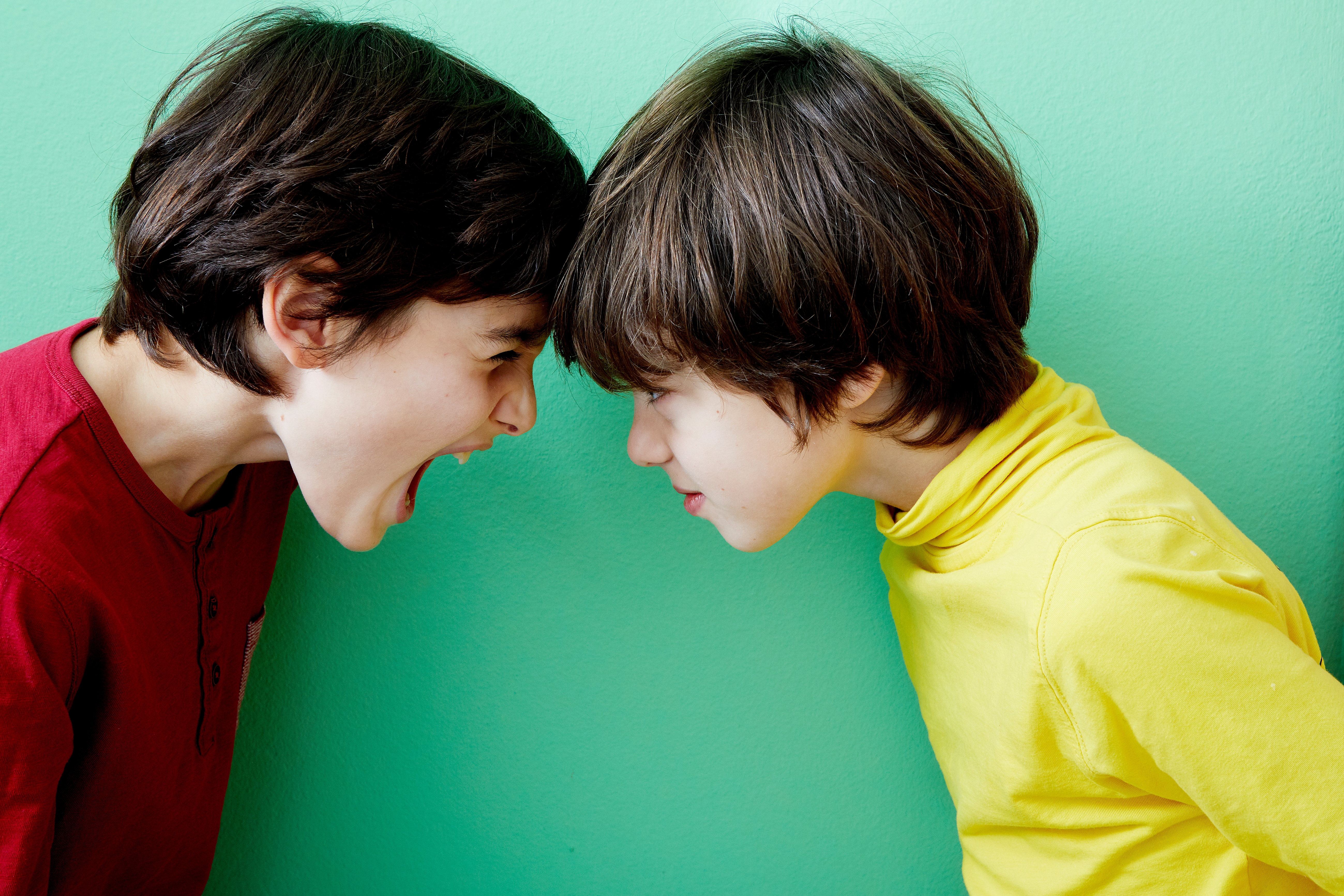 To barn som vender mot hverandre, den ene lekent roper, den andre smilende mykt, satt mot en enkel bakgrunn