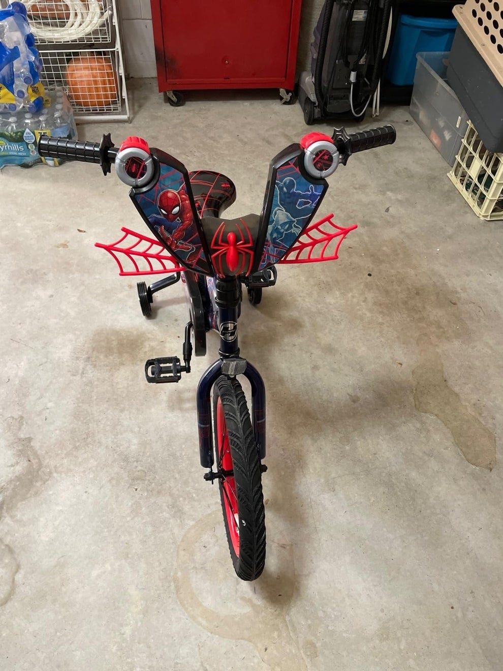 Child's bicycle with Spider-Man theme, featuring web accents and character motifs, parked on a garage floor