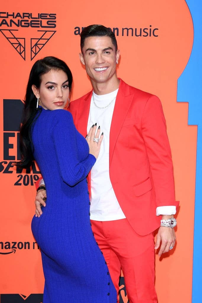 Two people on a red carpet; one in a bright suit and the other in a form-fitting dress, posing for photos