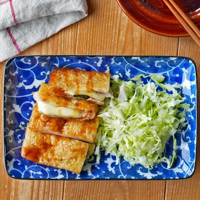青い皿に盛られた焼きたてのチーズ入り厚揚げと千切りキャベツ。横にはお箸が置かれている。