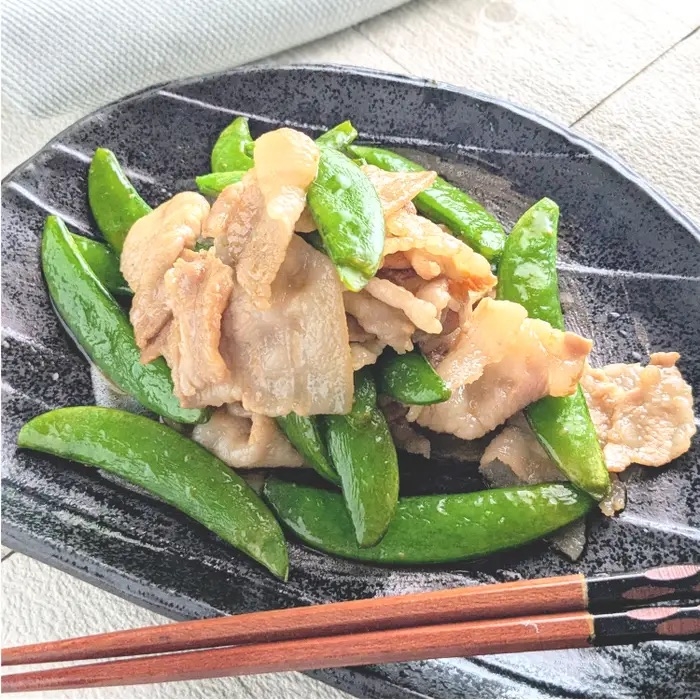 豚肉とスナップエンドウの炒め物が黒い皿に盛られている。横に箸が置かれている。