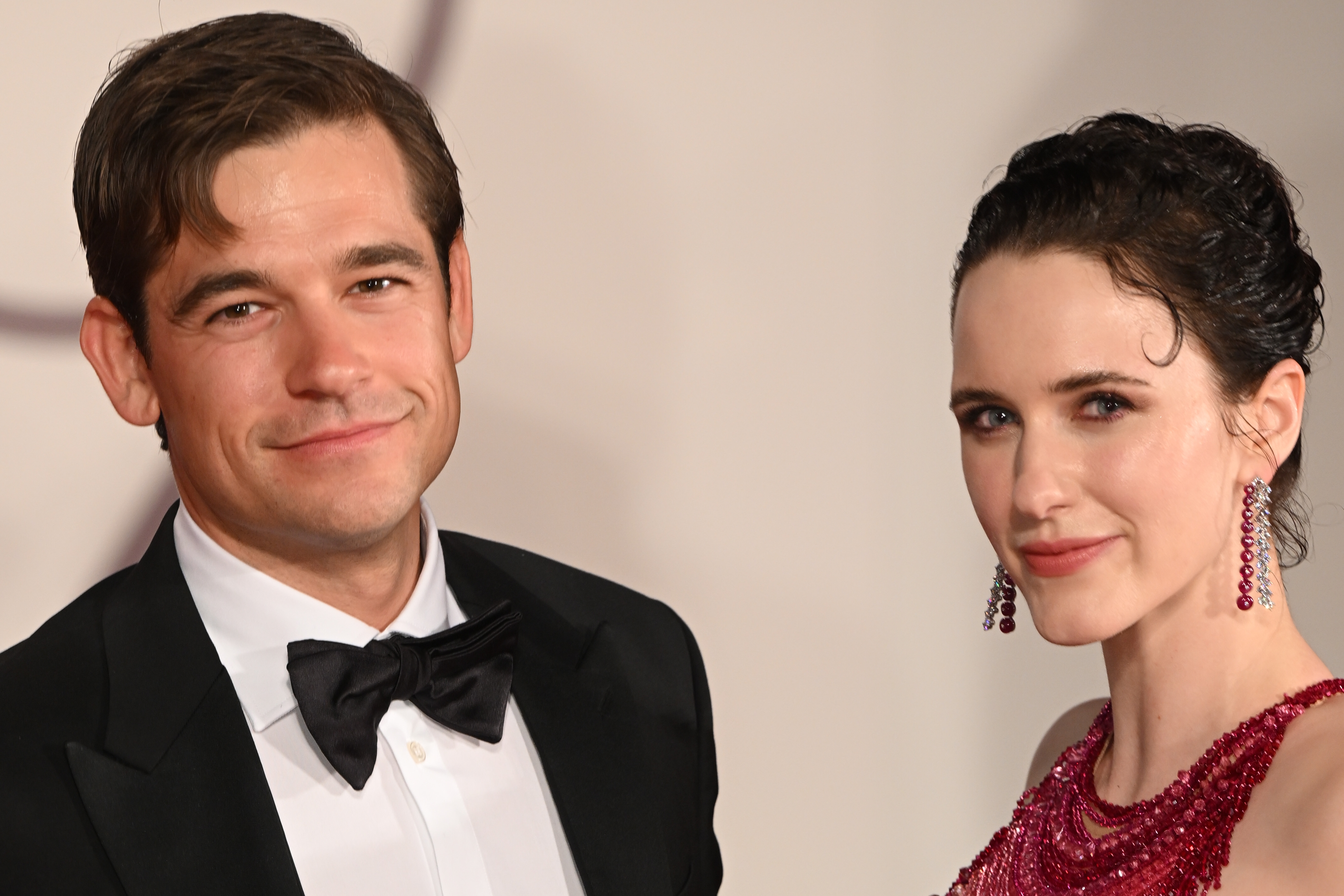 Jason Ralph in a tuxedo and Rachel Brosnahan in an elegant gown with jeweled earrings pose together at a formal event