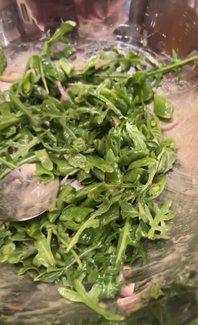A bowl of fresh arugula salad mixed with thinly sliced red onions and a dressing, with a spoon visible