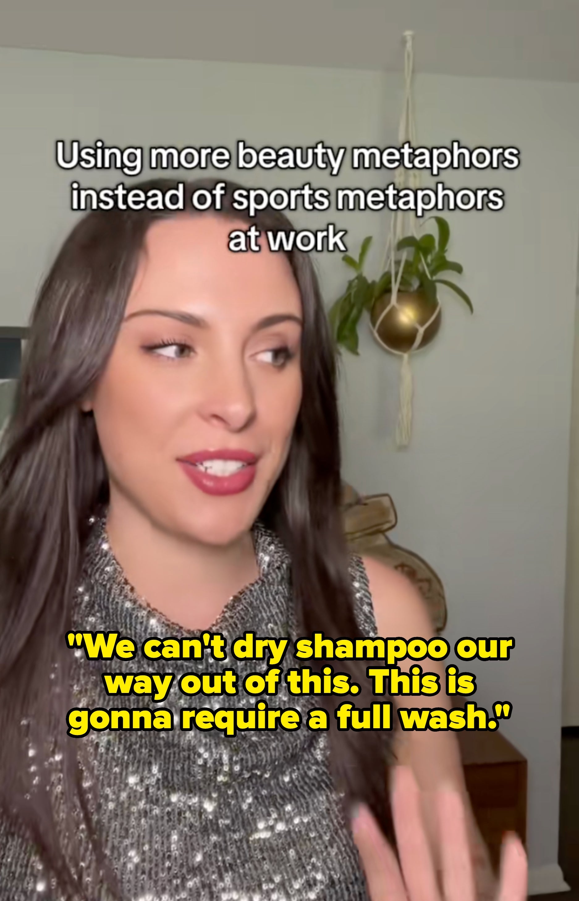 Kvinne i glitrende toppbevegelse mens du diskuterer skjønnhetsmetaforer for kommunikasjon på arbeidsplassen. Hengende plante i bakgrunnen