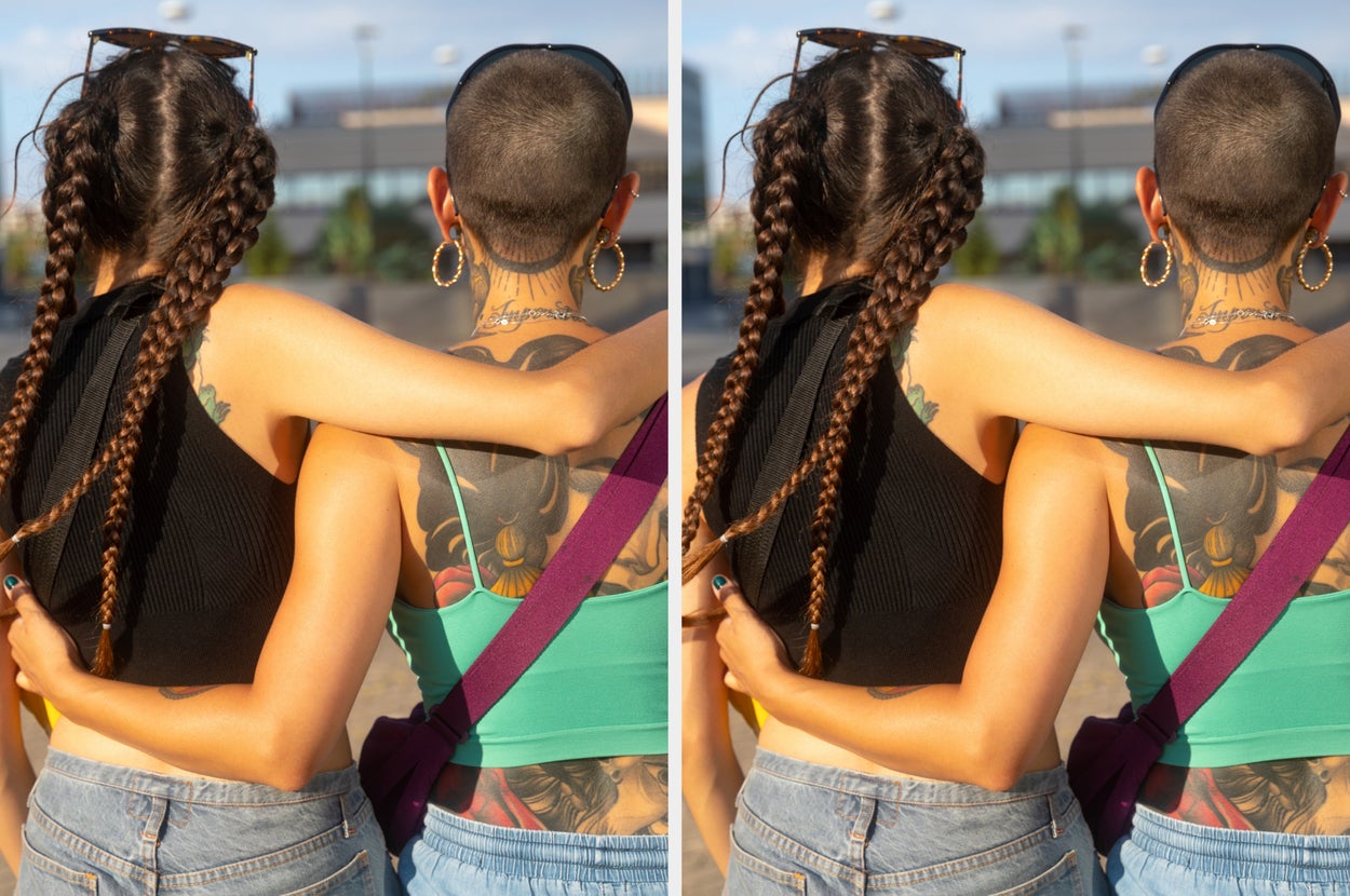 Two individuals with braided and shaved hairstyles, wearing casual tops and jeans, stand close with their arms over each other's shoulders outdoors