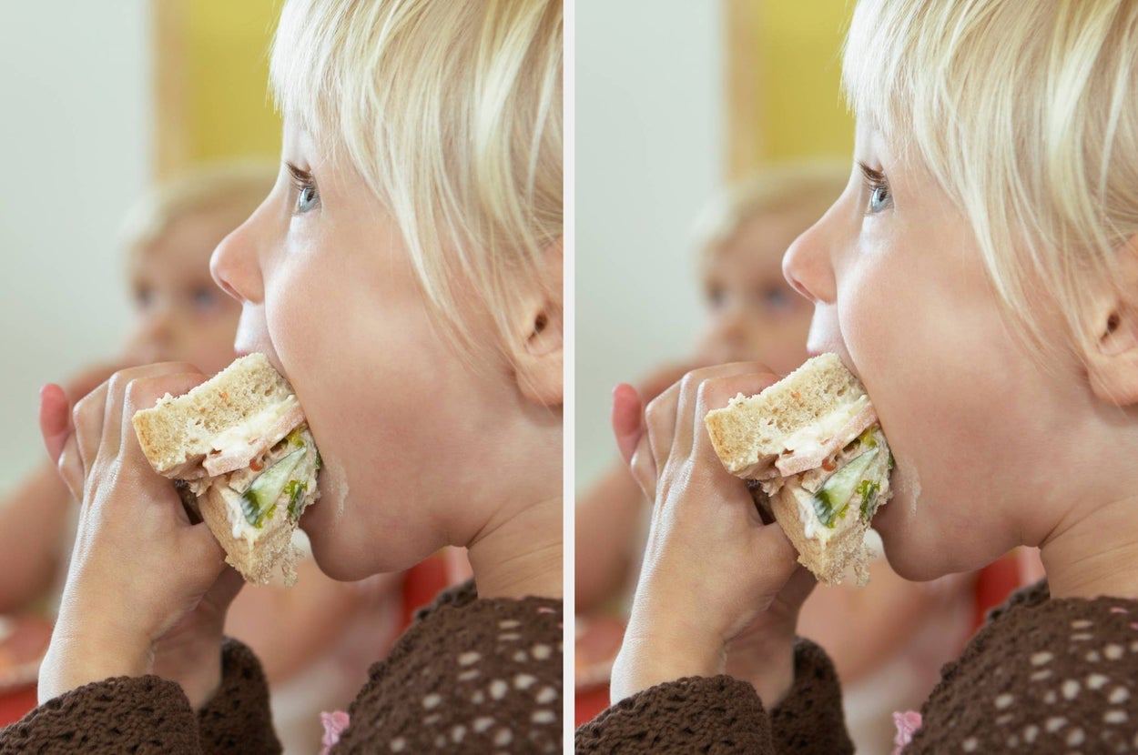 Child eating a sandwich filled with lettuce and tomato, with another person in the background