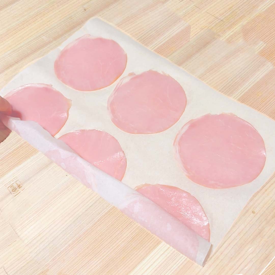 ハムのスライスがシート上に整然と並べられている様子。シートの端がめくられている。