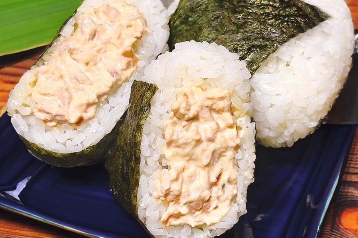 2つのツナマヨおにぎりが青い皿に並んでいる。海苔で包まれたご飯の中にツナマヨが入っている。