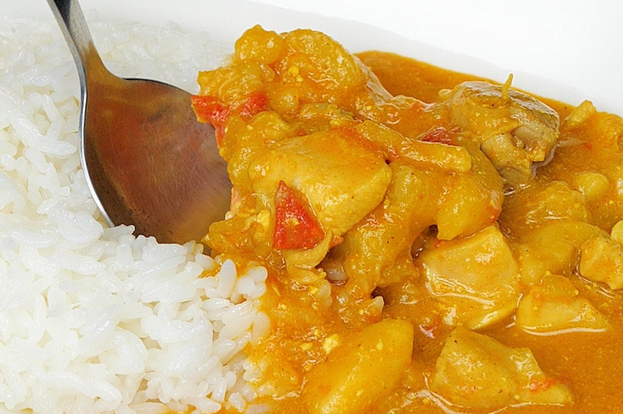 白い皿にサーブされたカレーとご飯をスプーンで食べる様子。