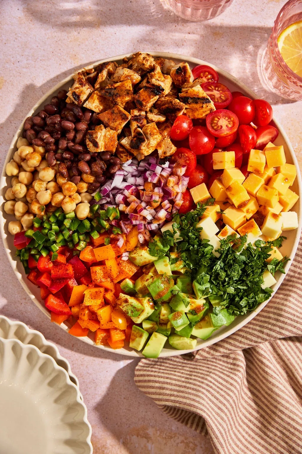 Platter with grilled chicken, cherry tomatoes, black beans, chickpeas, cheese, avocado, peppers, red onion, and cilantro, neatly arranged