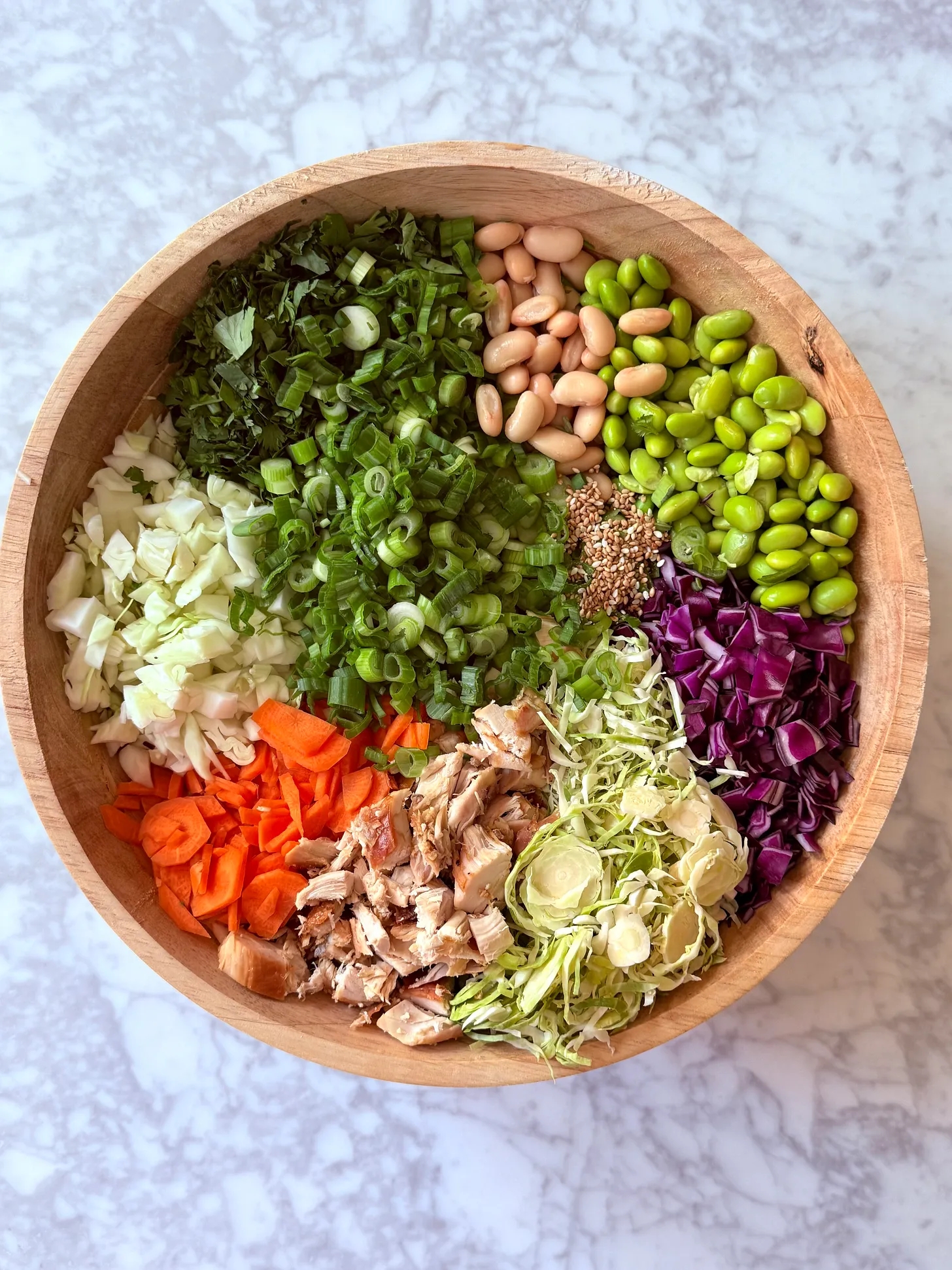 A wooden bowl filled with various chopped vegetables, beans, and greens arranged in separate sections, creating a colorful display