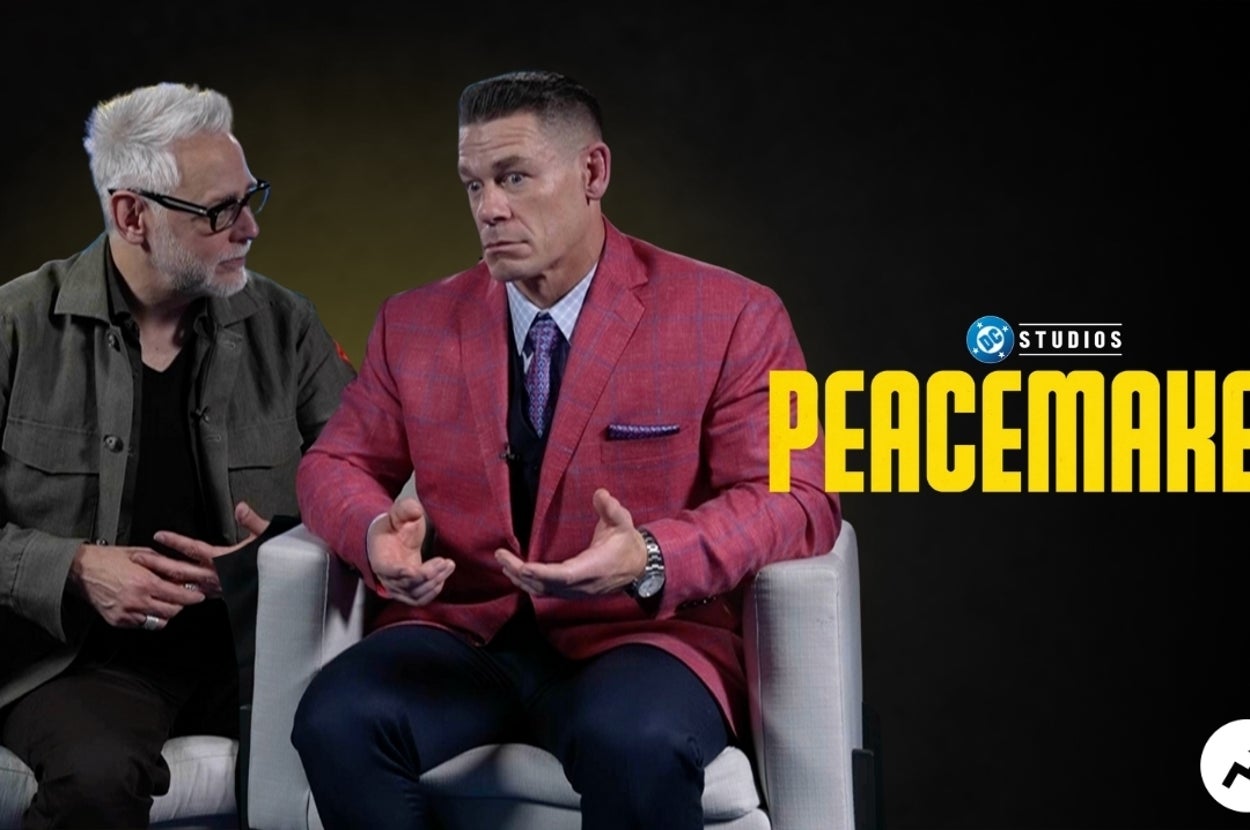 Dos personas sentadas, una con chaqueta casual, la otra con traje rojo. Al fondo se ve "Peacemaker" escrito