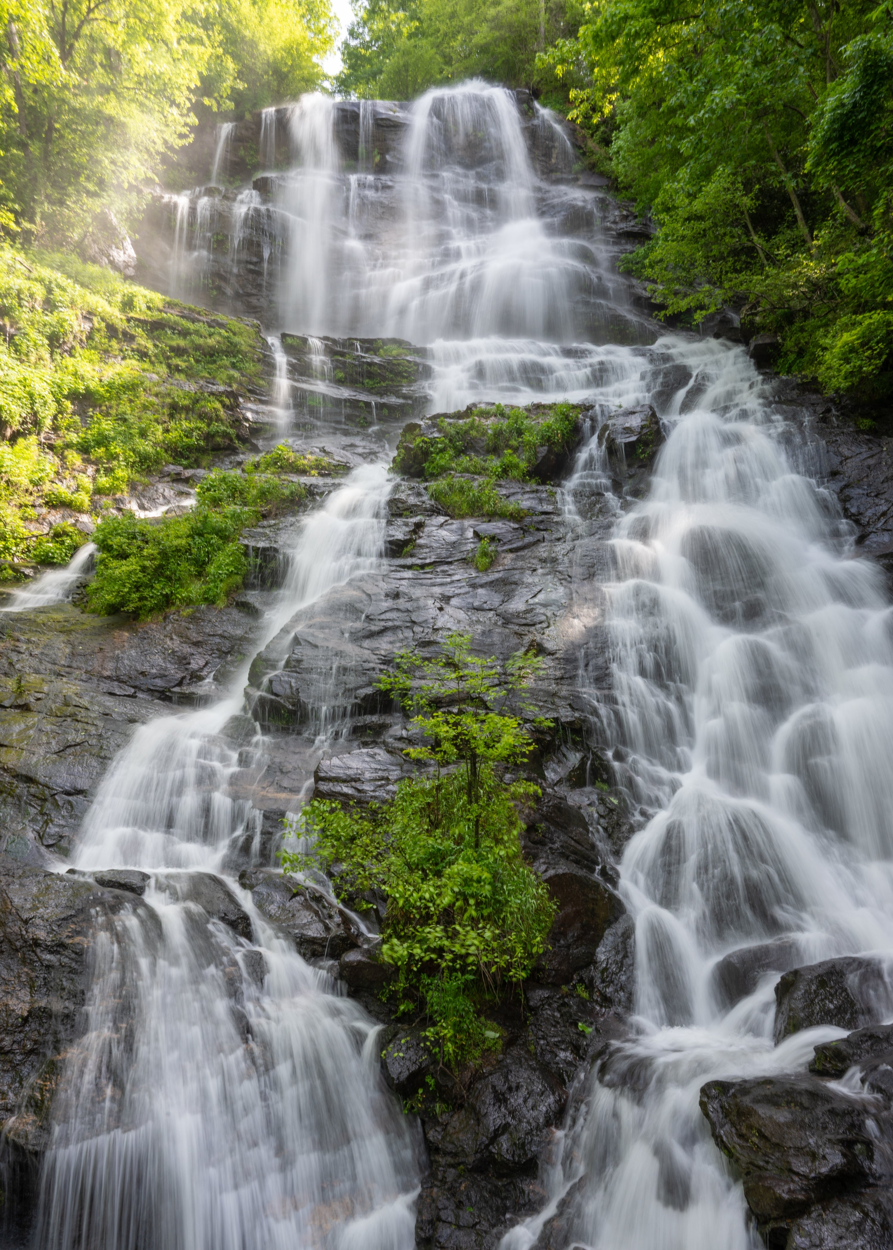 Vann kaskader nedover en steinete foss omgitt av frodig grønt løvverk