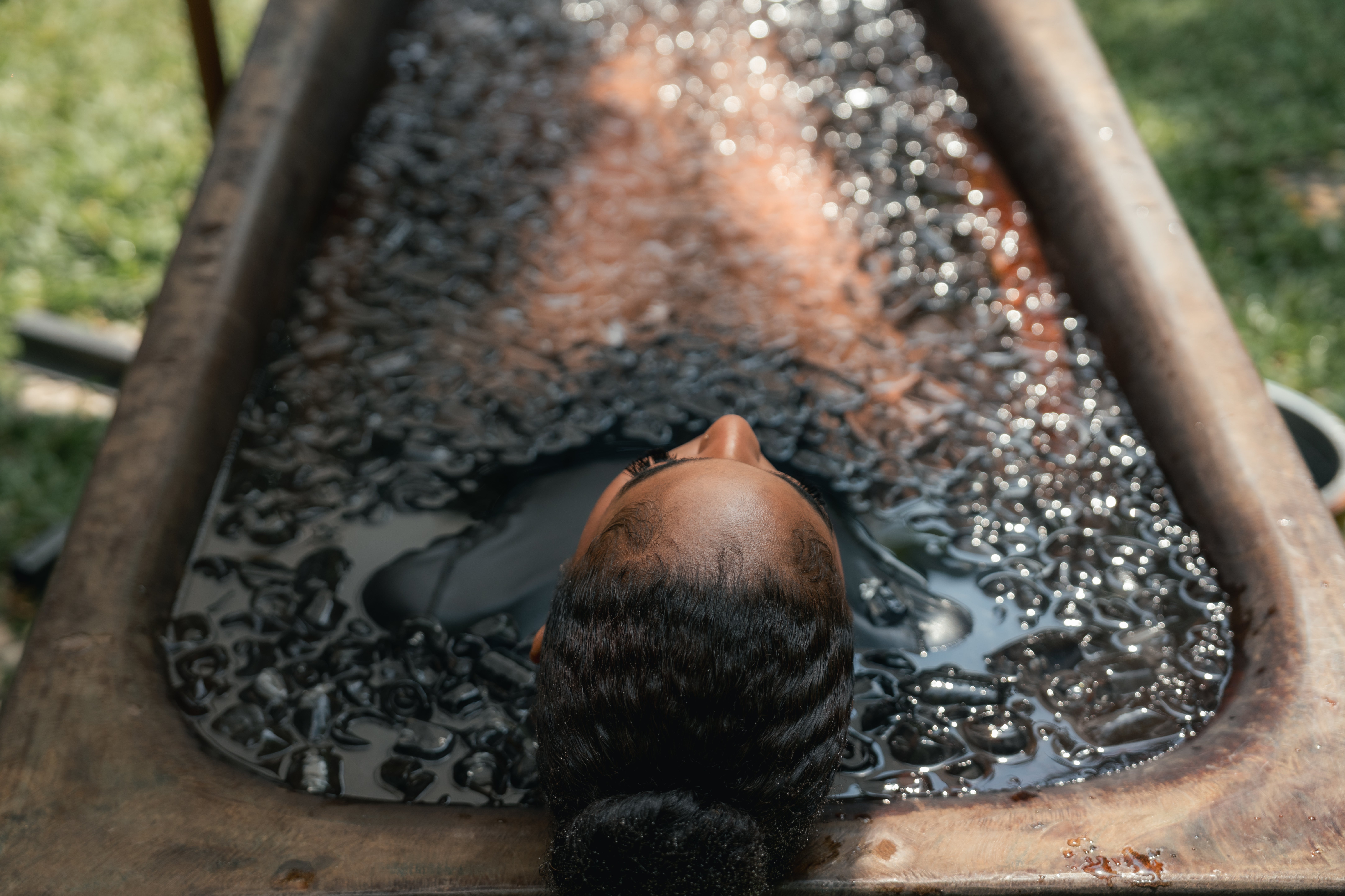 Personen ligger i et isfylt kar, hodet over vann, utendørs. Avslappet holdning