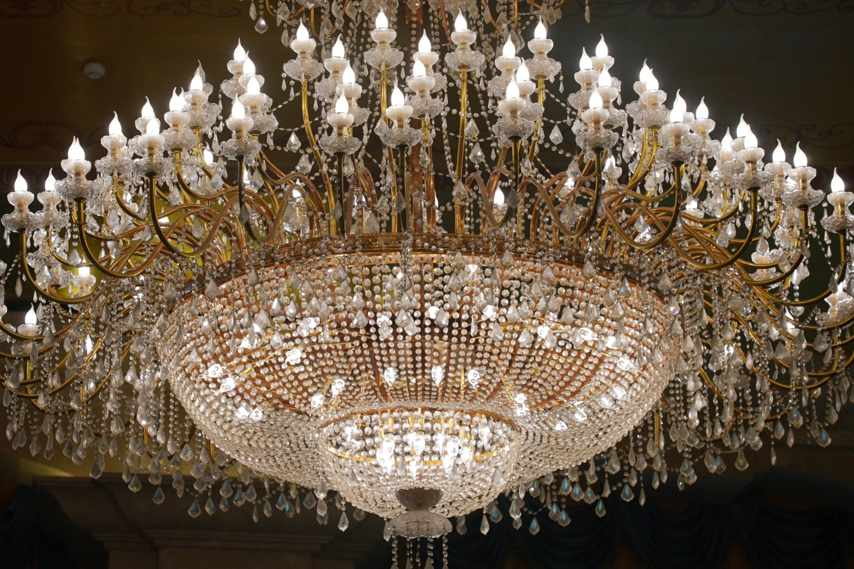 Large ornate chandelier with numerous lights and intricate crystal decorations hangs from the ceiling, creating a luxurious atmosphere