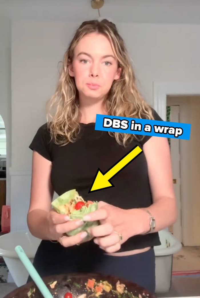 Person holding a lettuce wrap with a mix of vegetables and chicken in a kitchen setting