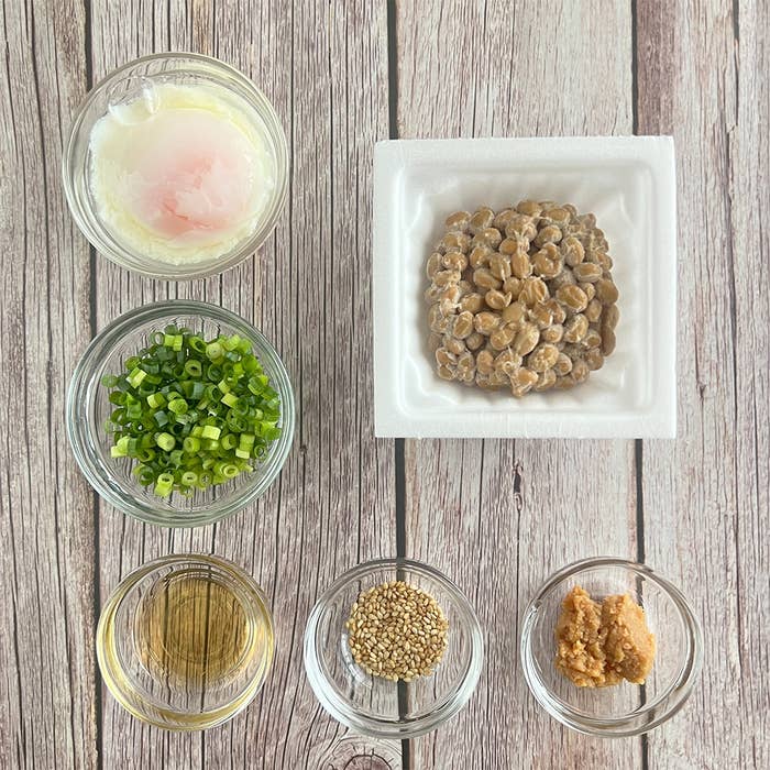 温泉卵、納豆、ネギ、ごま、味噌、調味料が並ぶテーブル。調理前の食材準備。