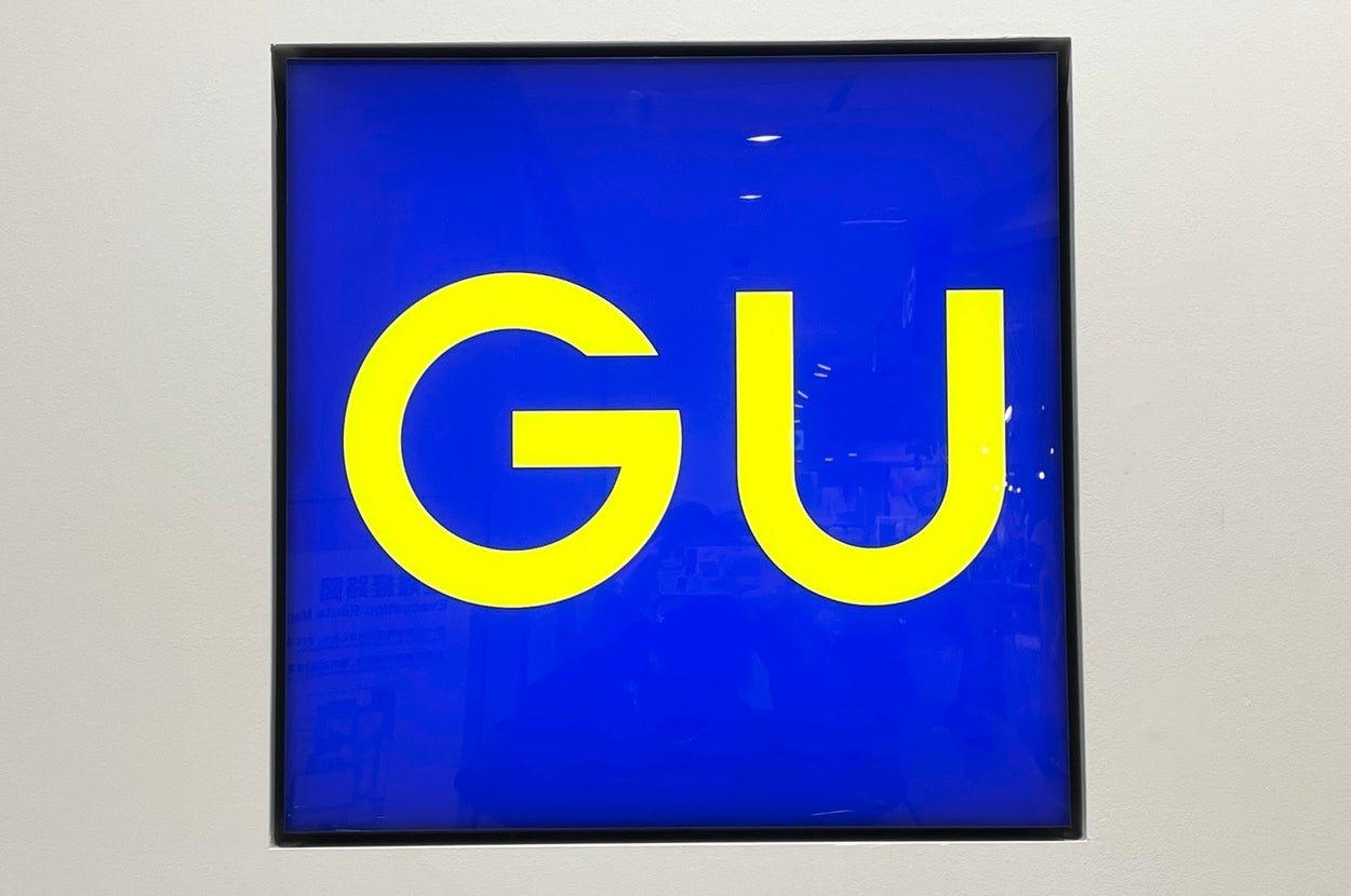 The image shows a sign with the bold letters "GU" on a blue background