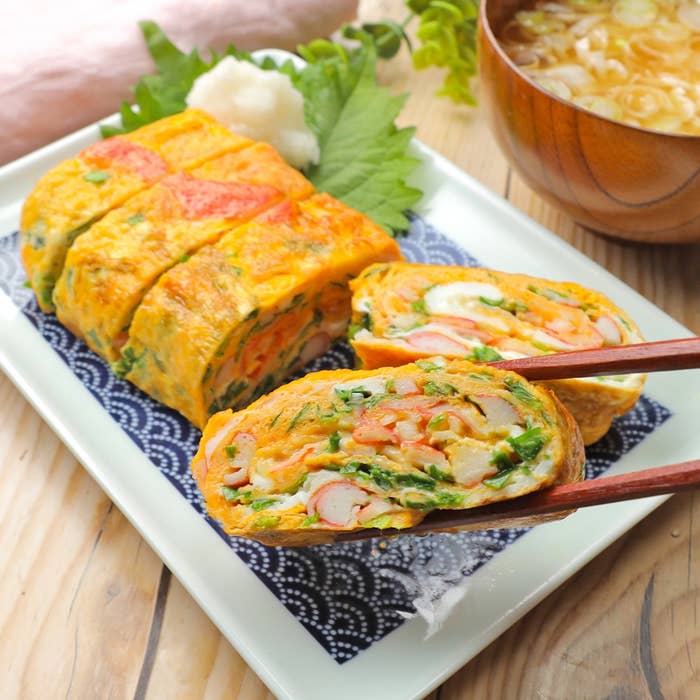卵焼きが皿に盛られており、野菜やかにかまが入っています。添え物と味噌汁もあります。