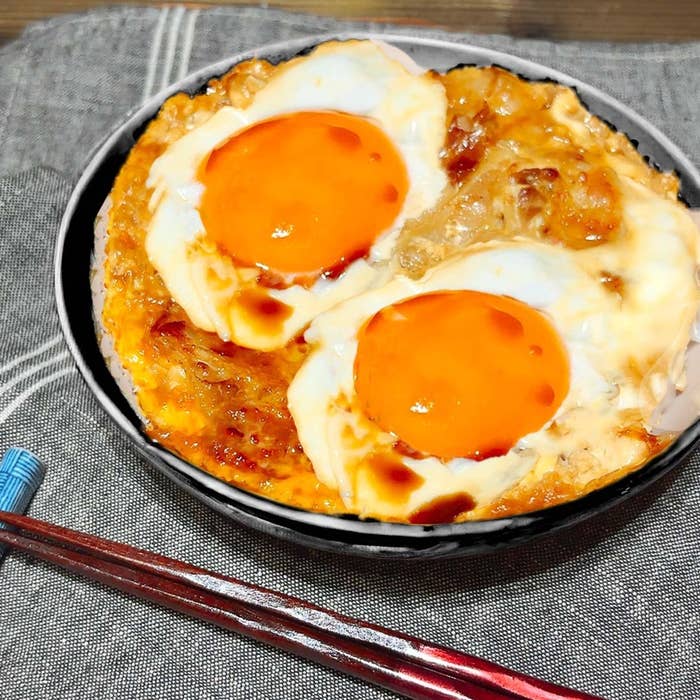 目玉焼きが載った丼ぶりご飯。赤い箸が置かれている。